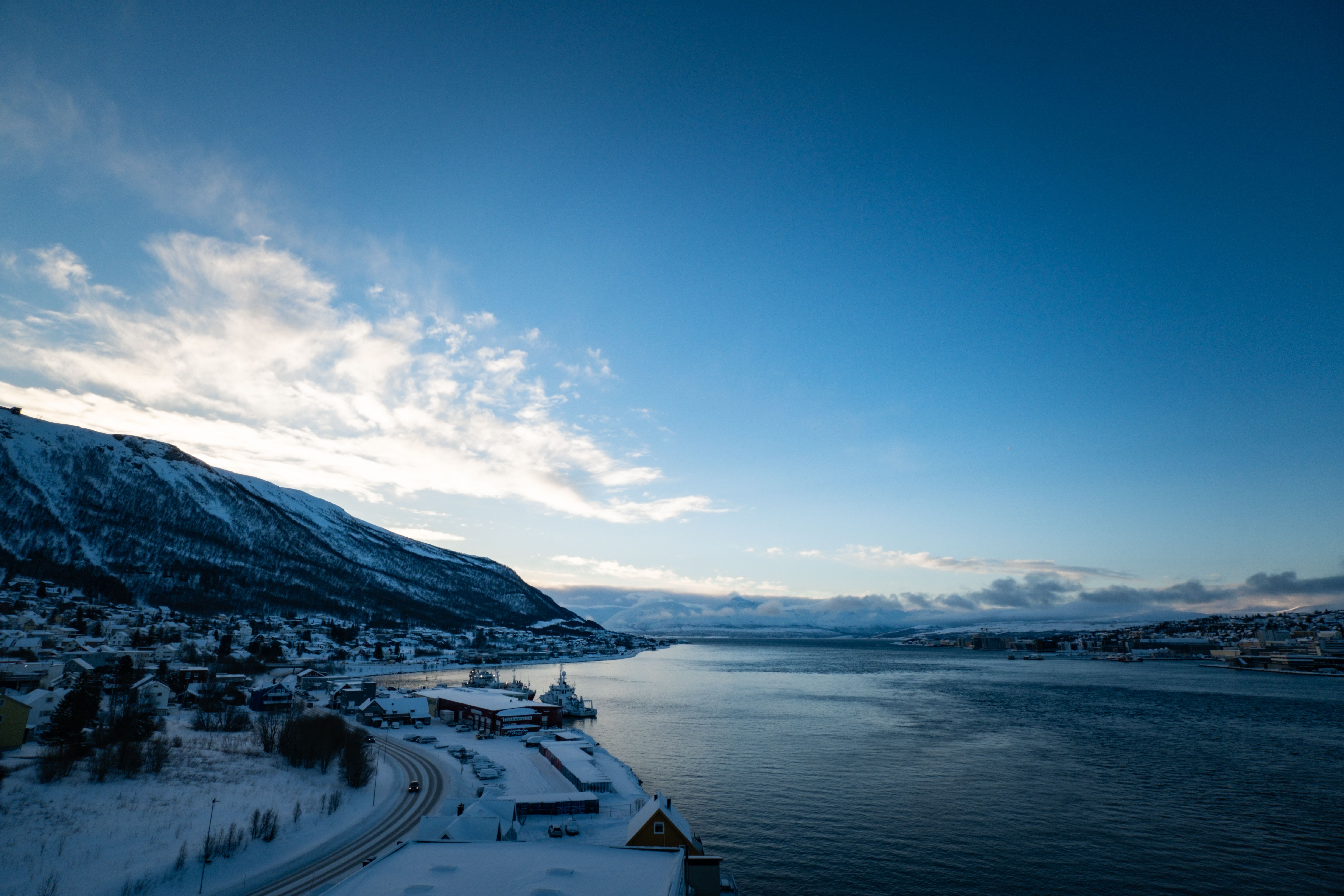 Aerial view of a snowy fjord landscape in Northern Norway during winter. Serene ocean and mountains under a clear sky.
