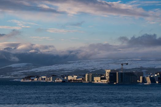 Majestic winter scene of a coastal town surrounded by snow-covered mountains and sea.