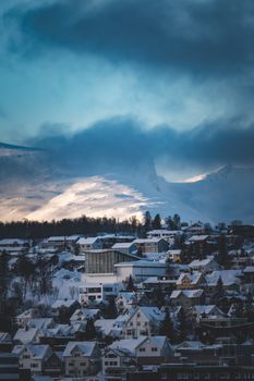 A stunning aerial view of a town blanketed in snow with mountains in the background, capturing a serene winter landscape.