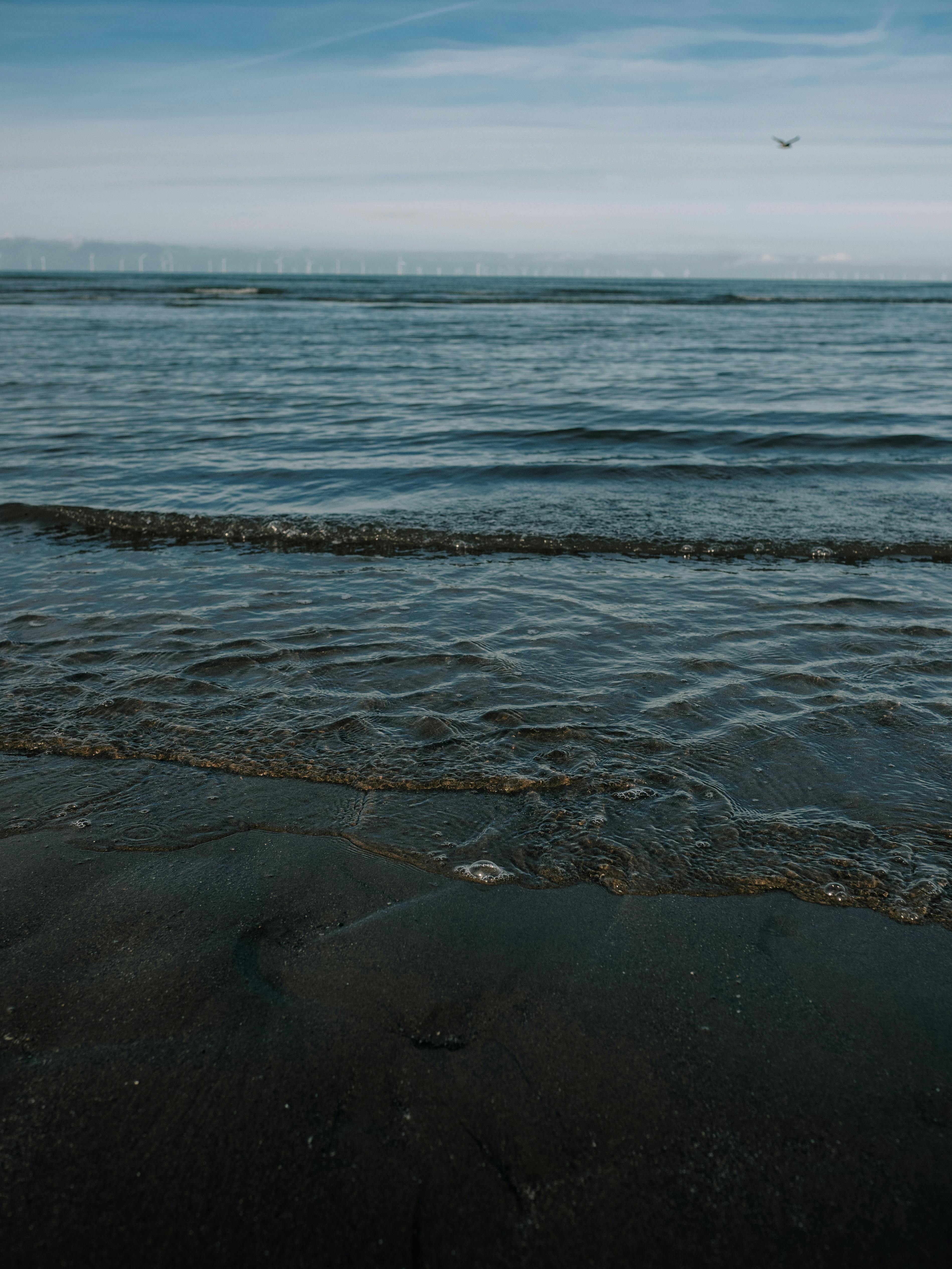 Tranquil view of ocean waves gently lapping at a sandy shore under a serene sky.