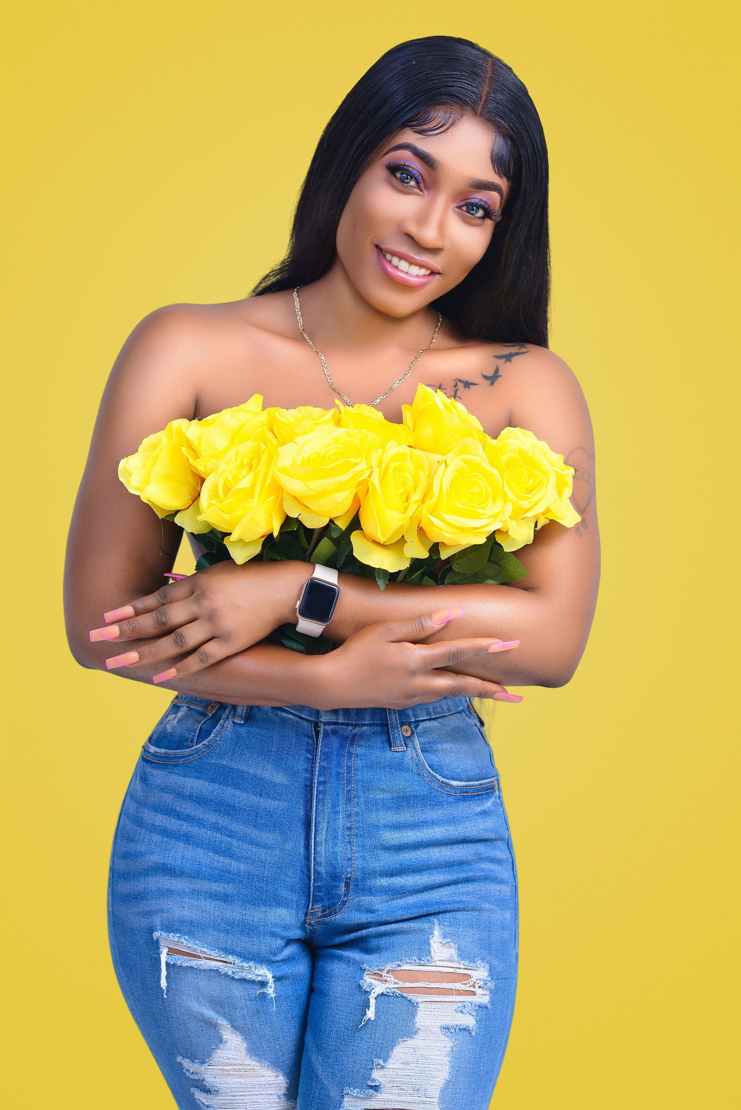 Fashionable portrait of a smiling woman holding yellow roses on a yellow background.