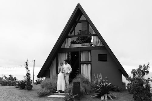 A black and white photo of a couple standing in front of a triangular shaped house