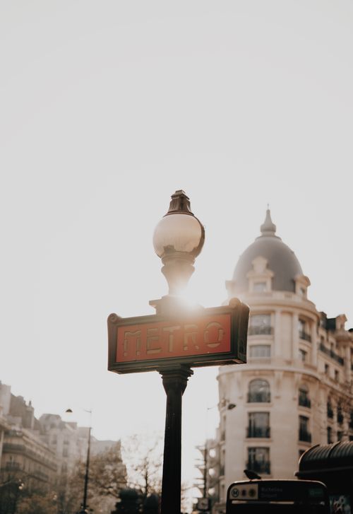 Free A Paris metro sign with a sun flare, framed by classic Parisian architecture. Stock Photo