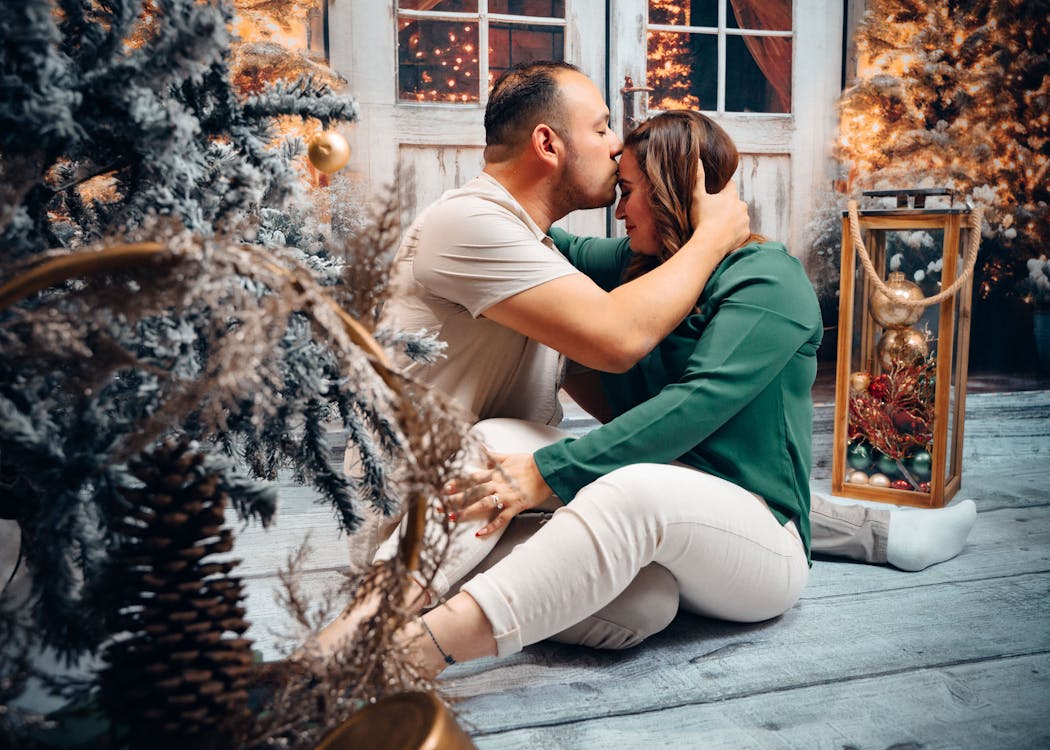 Young Couple Sitting on a Floor among Christmas Decorations and Kissing 