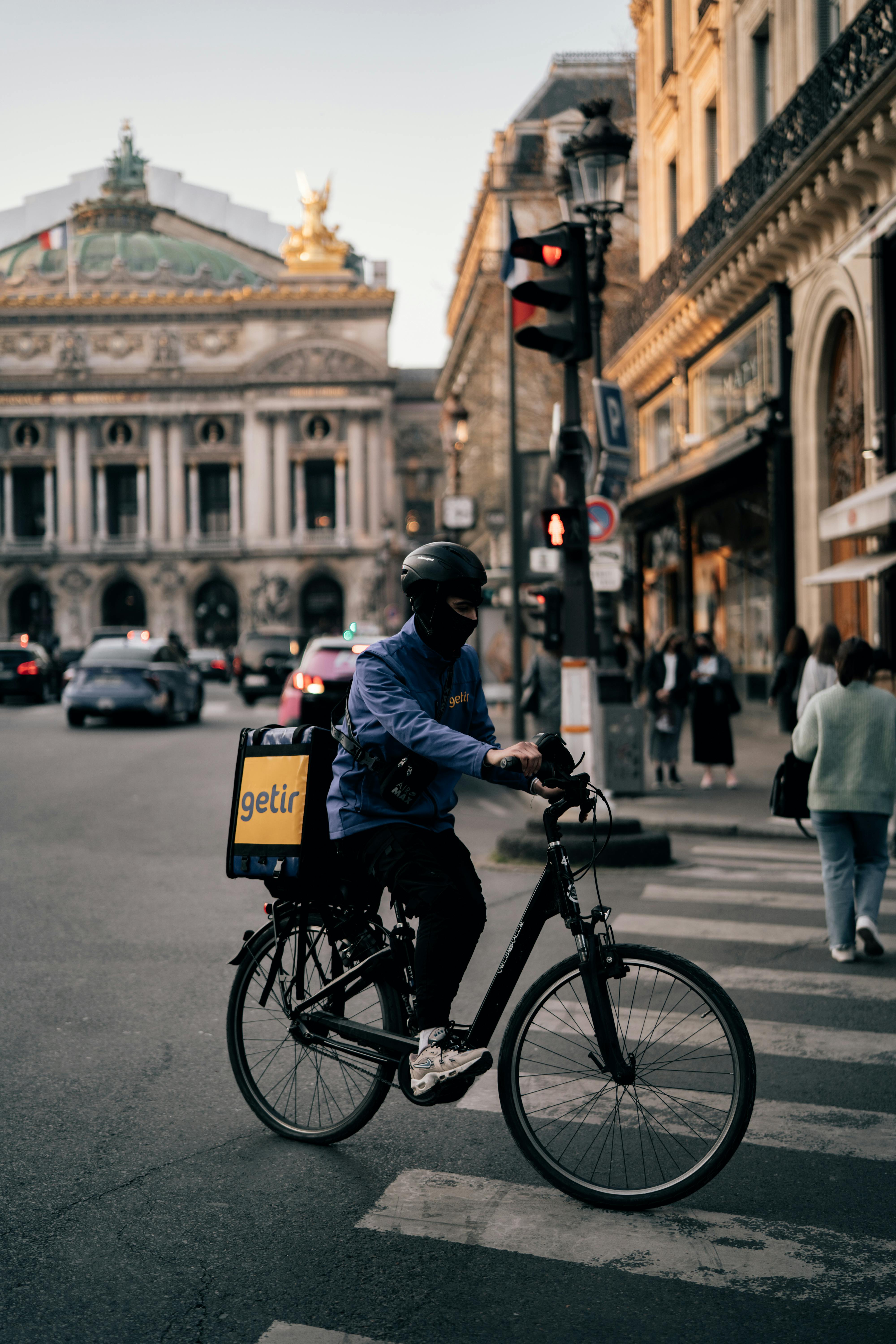 Courier on a bicycle in front of the iconic Palais Garnier in Paris.