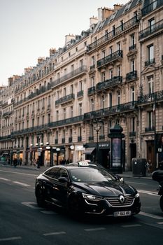 Taxi driving past historic buildings on a Parisian street, capturing urban charm and architecture.