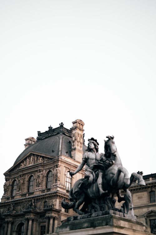 Free Elegant statue beside the historic Louvre Palace in Paris, showcasing classic architectural details. Stock Photo
