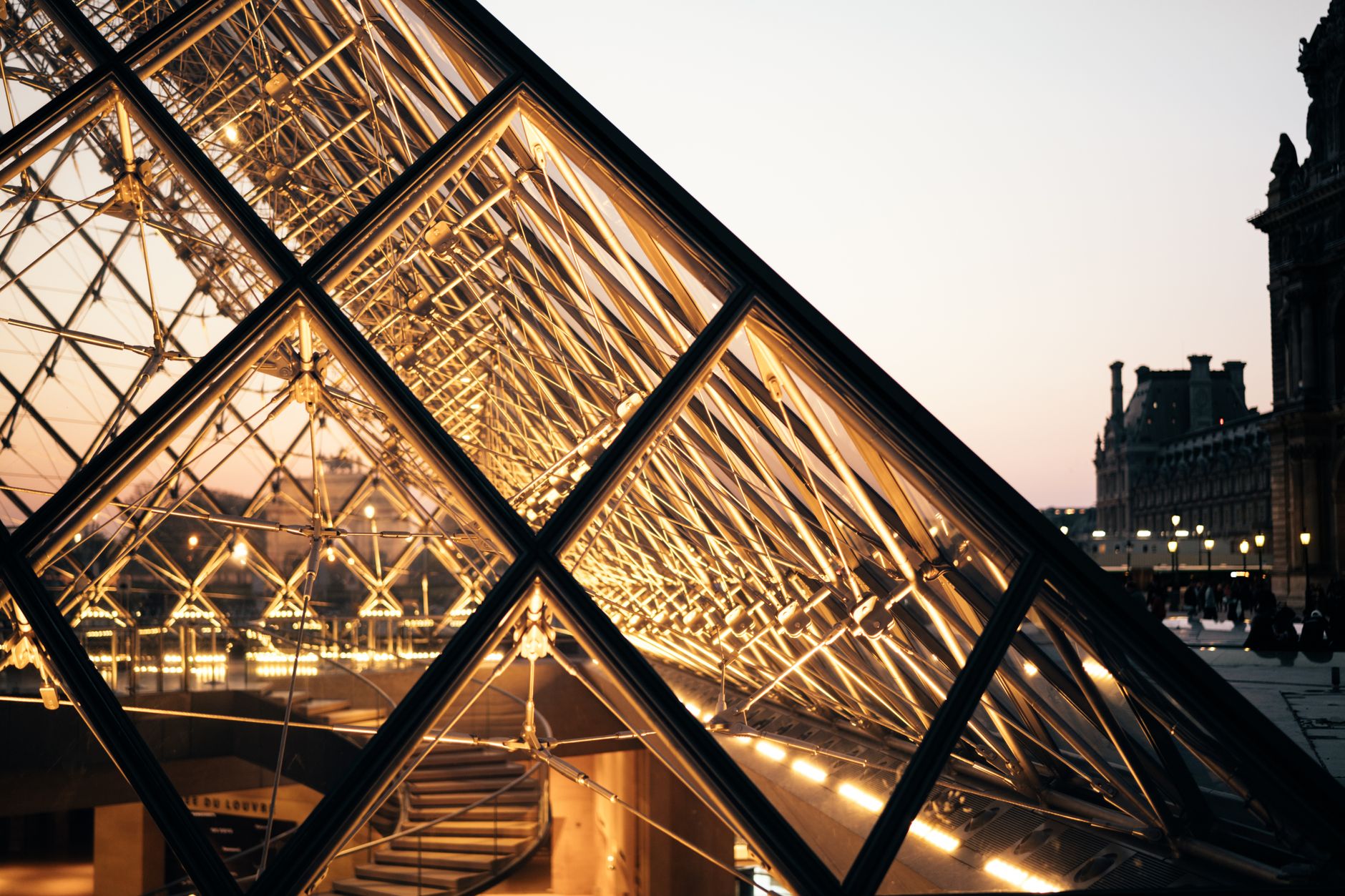A beautiful evening shot of the Louvre Pyramid in Paris, showcasing modern architecture and reflections.