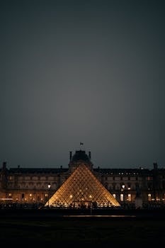 A stunning night view of the Louvre Pyramid glowing warmly against the historic facade in Paris.