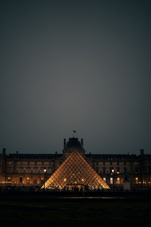 Free A stunning night view of the Louvre Pyramid glowing warmly against the historic facade in Paris. Stock Photo