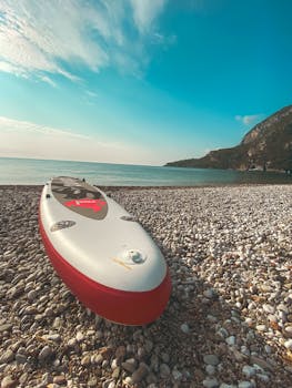 Standup paddleboard resting on a pebble beach with a scenic coastal view in Kemer, Antalya.