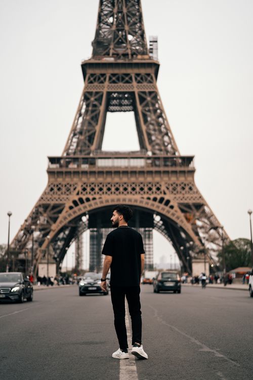 Free Man walking on a street towards the iconic Eiffel Tower in Paris, France, during the day. Stock Photo