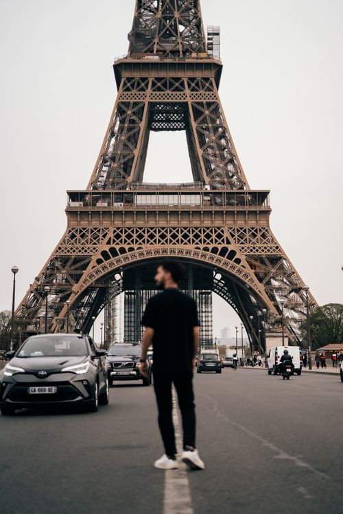Free A vibrant street view of the Eiffel Tower with a pedestrian walking by, capturing urban life in Paris. Stock Photo
