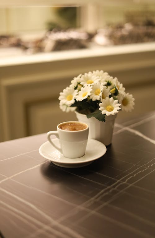 Cup of Coffee Next to a Pot of Artificial Flowers