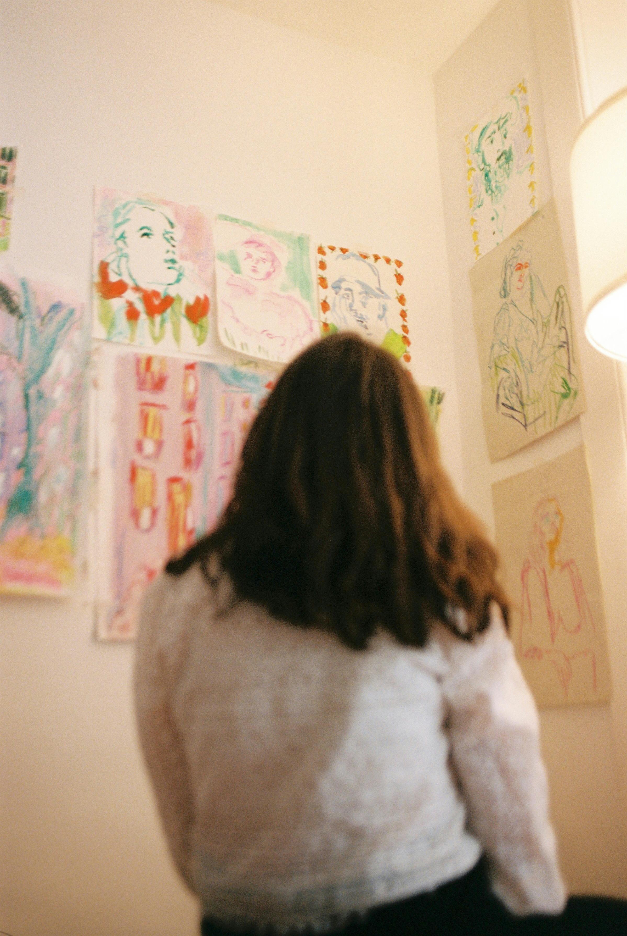 Woman observing colorful art sketches on a wall in a well-lit room.