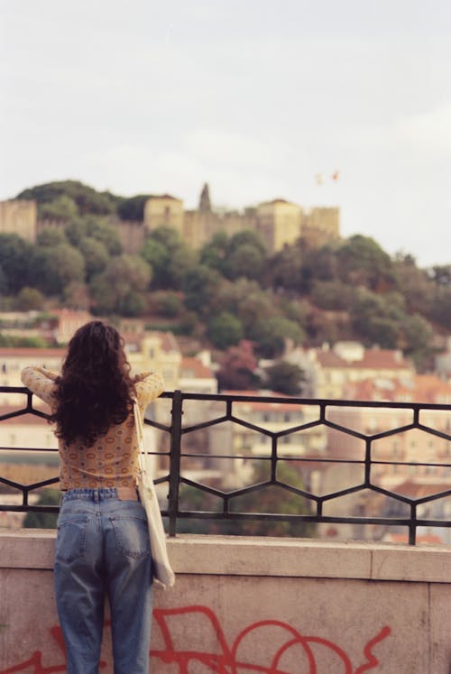 Woman Leaning on a Railing and Looking at a View of a City 