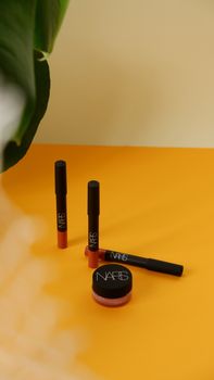 NARS makeup products on a yellow surface, featuring lipsticks and jar.
