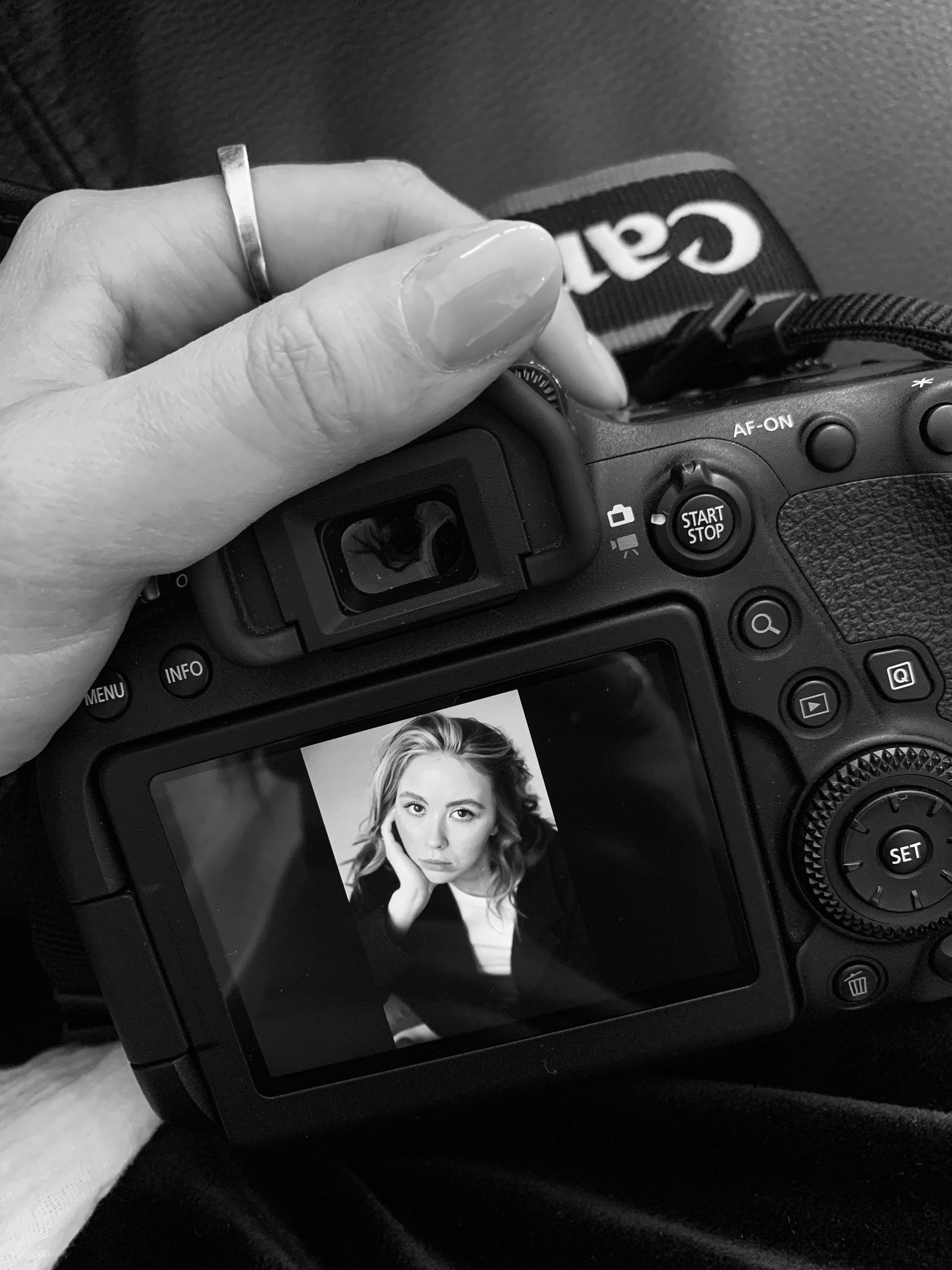 Ruka držící DSLR fotoaparát zobrazující černobílý obraz, na obrazovce portrét ženy.