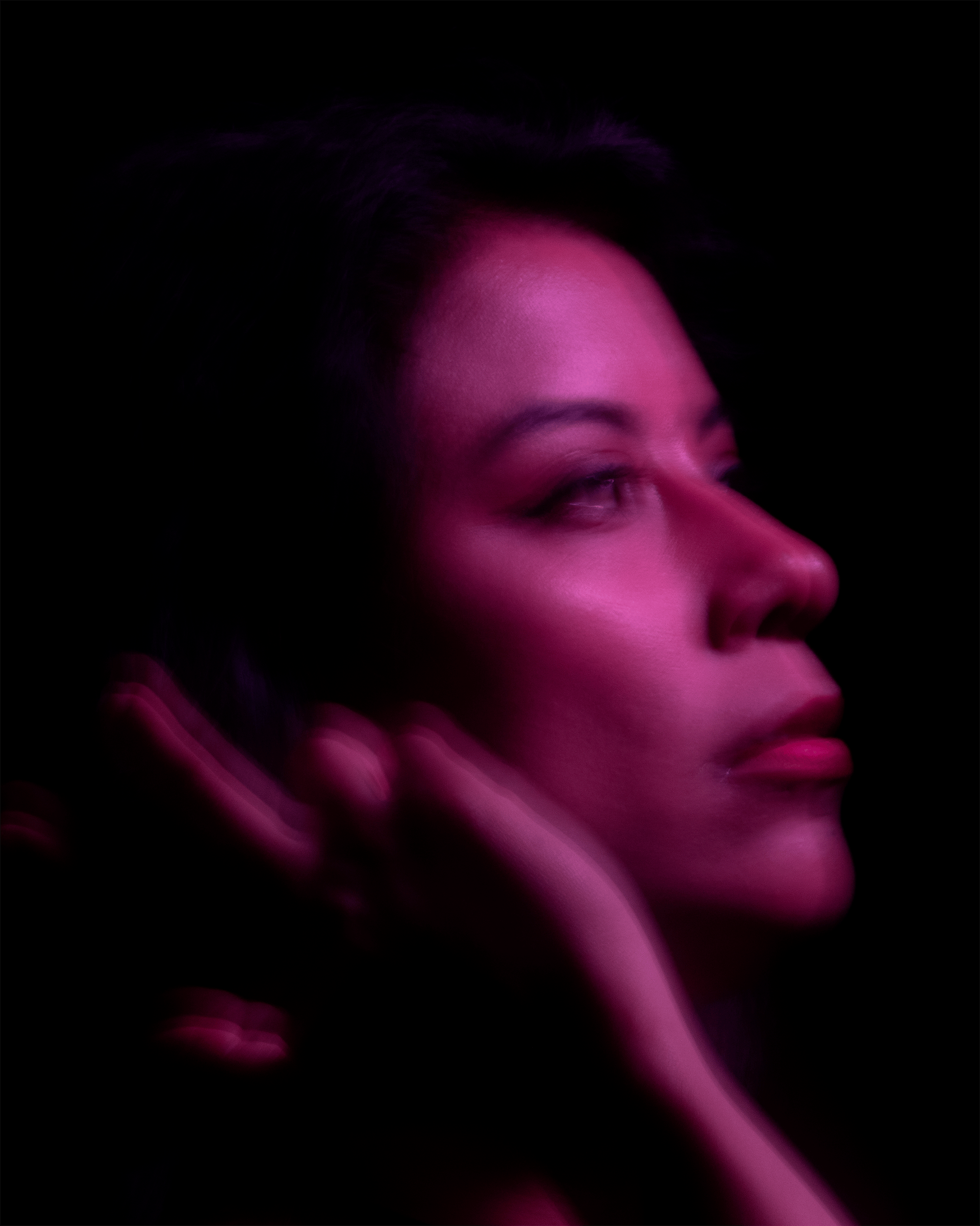 Artistic portrait of a woman in soft, pink lighting with a defocused background.