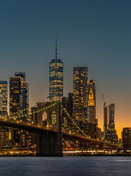 Stunning view of Brooklyn Bridge leading to illuminated Manhattan skyline at sunset