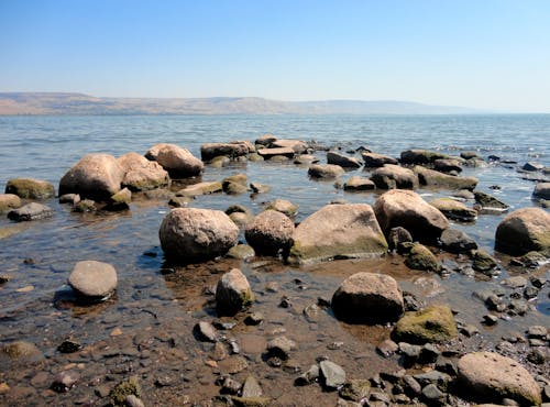 Detail of rocky shore of Sea of Galilee in Israel. Water and blue sky landscape with hills in the background