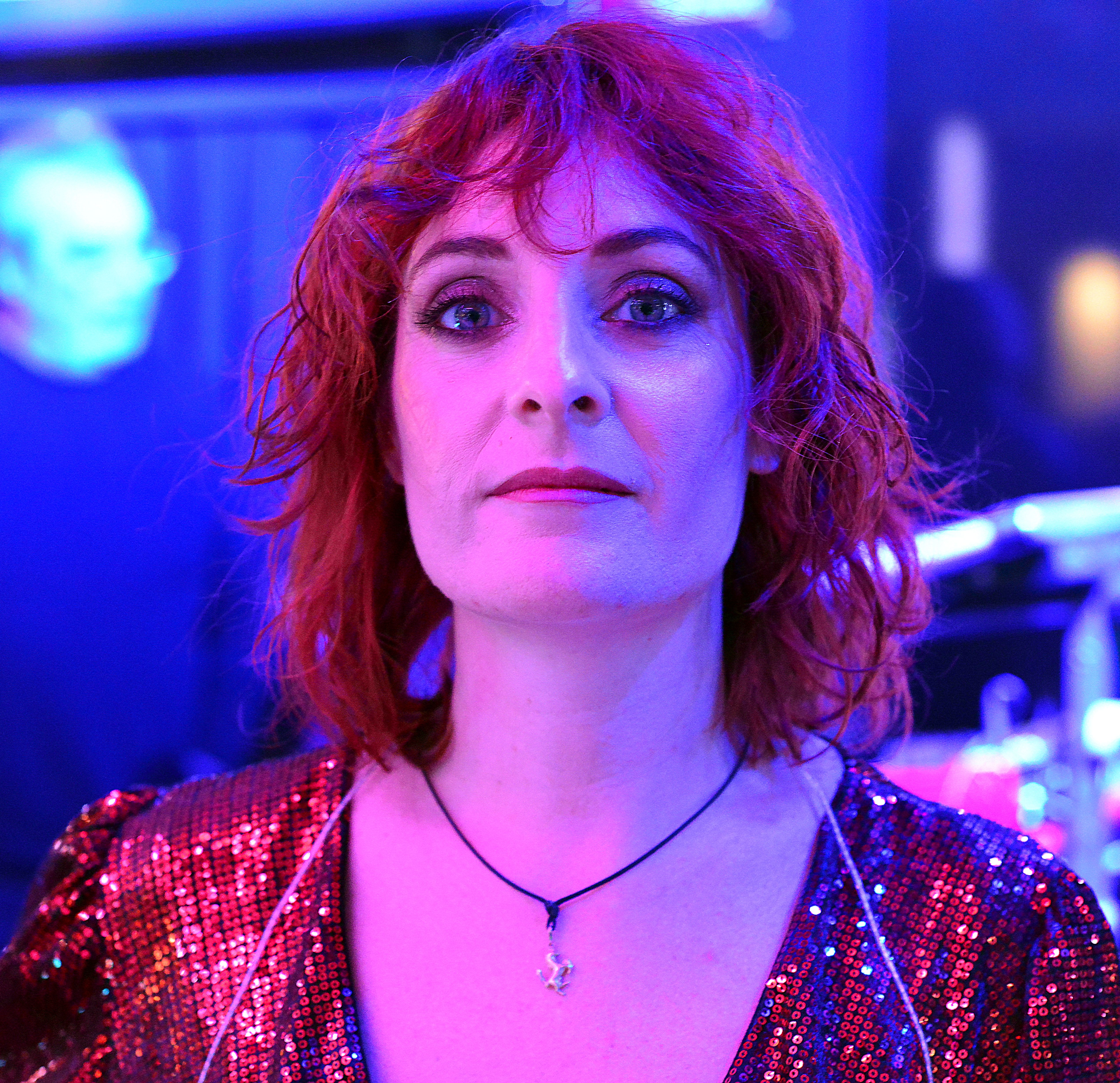 Close-up portrait of a woman with red hair and sequin outfit under pink lighting.