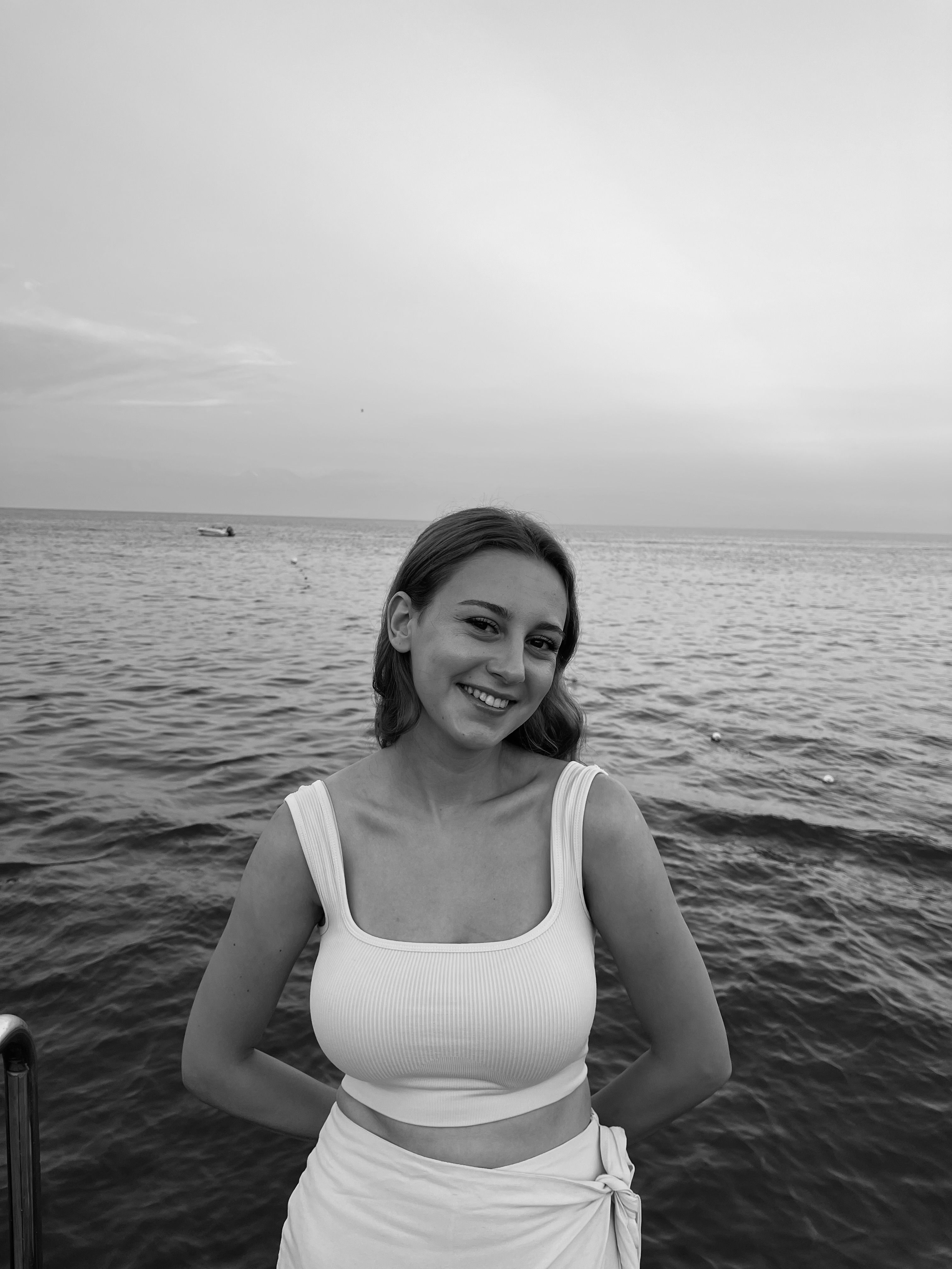 Black and white portrait of a smiling woman at the shore in Kemer, Türkiye, showcasing fashion and serenity.