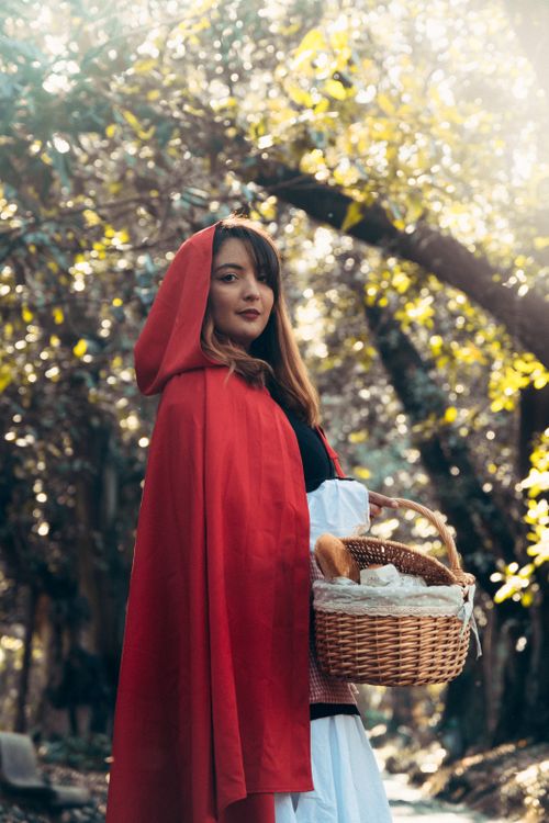 Free Portrait of a woman in a red cloak holding a basket, reminiscent of Little Red Riding Hood, in an outdoor forest setting. Stock Photo