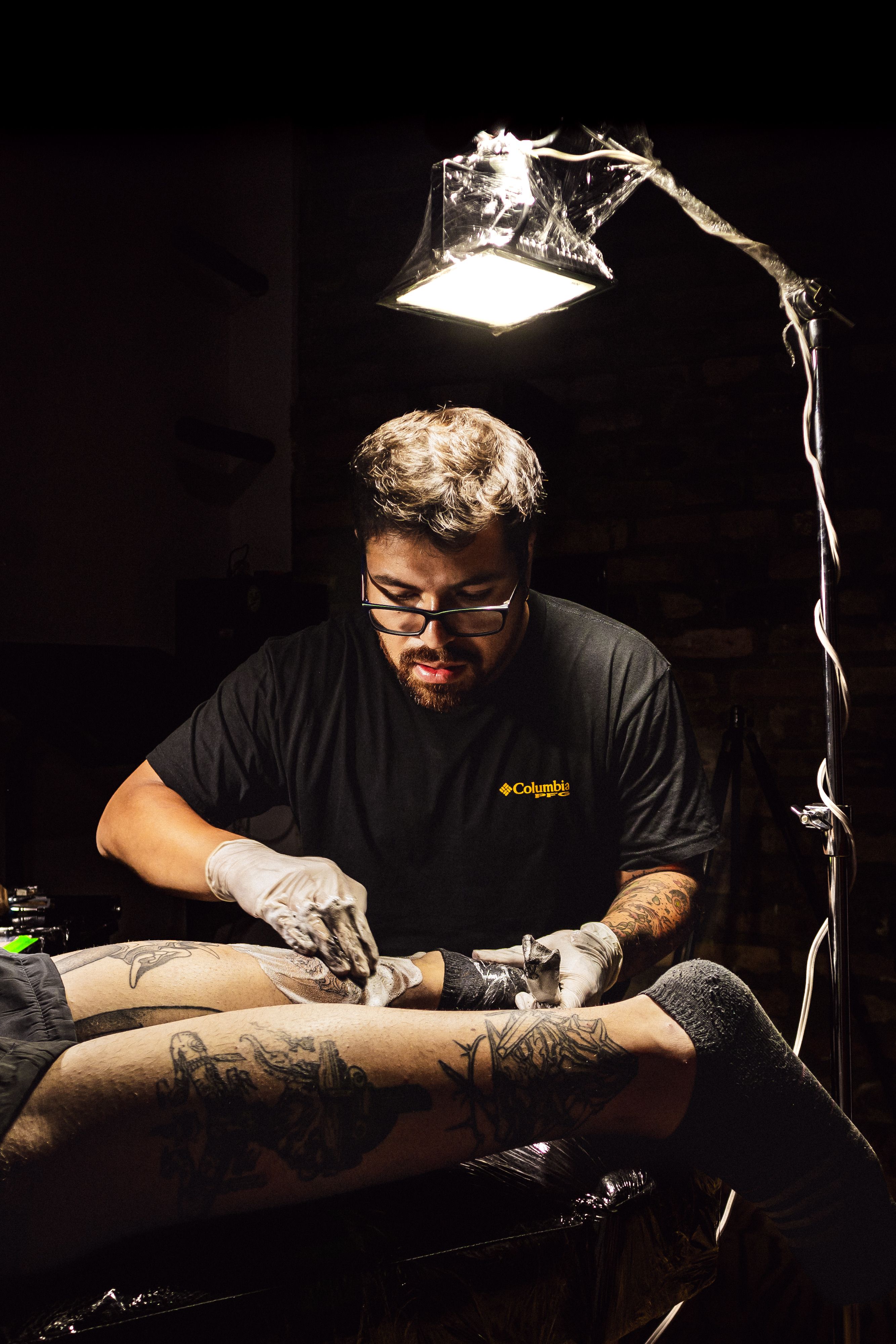 Tattoo artist in Popayán, Cauca, Colombia, intricately designs leg tattoos in studio.