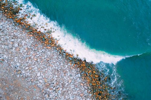 Free Captivating aerial view of turquoise waves crashing on a rocky beach shore. Stock Photo
