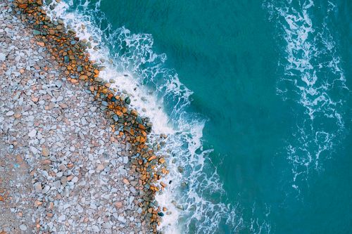 Free A stunning aerial photograph capturing the contrast of rocky shore and vibrant ocean waves. Stock Photo