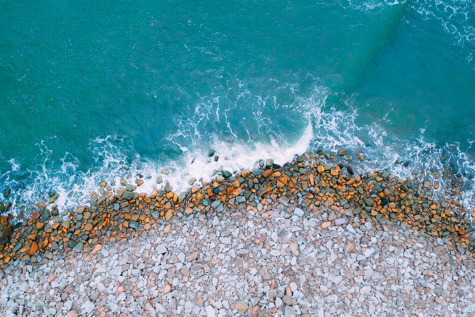 A stunning aerial view capturing the contrast between rocky shores and azure ocean waves.
