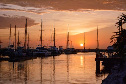 Free A tranquil marina setting at sunset with yachts moored, reflecting on the calm sea waters. Stock Photo