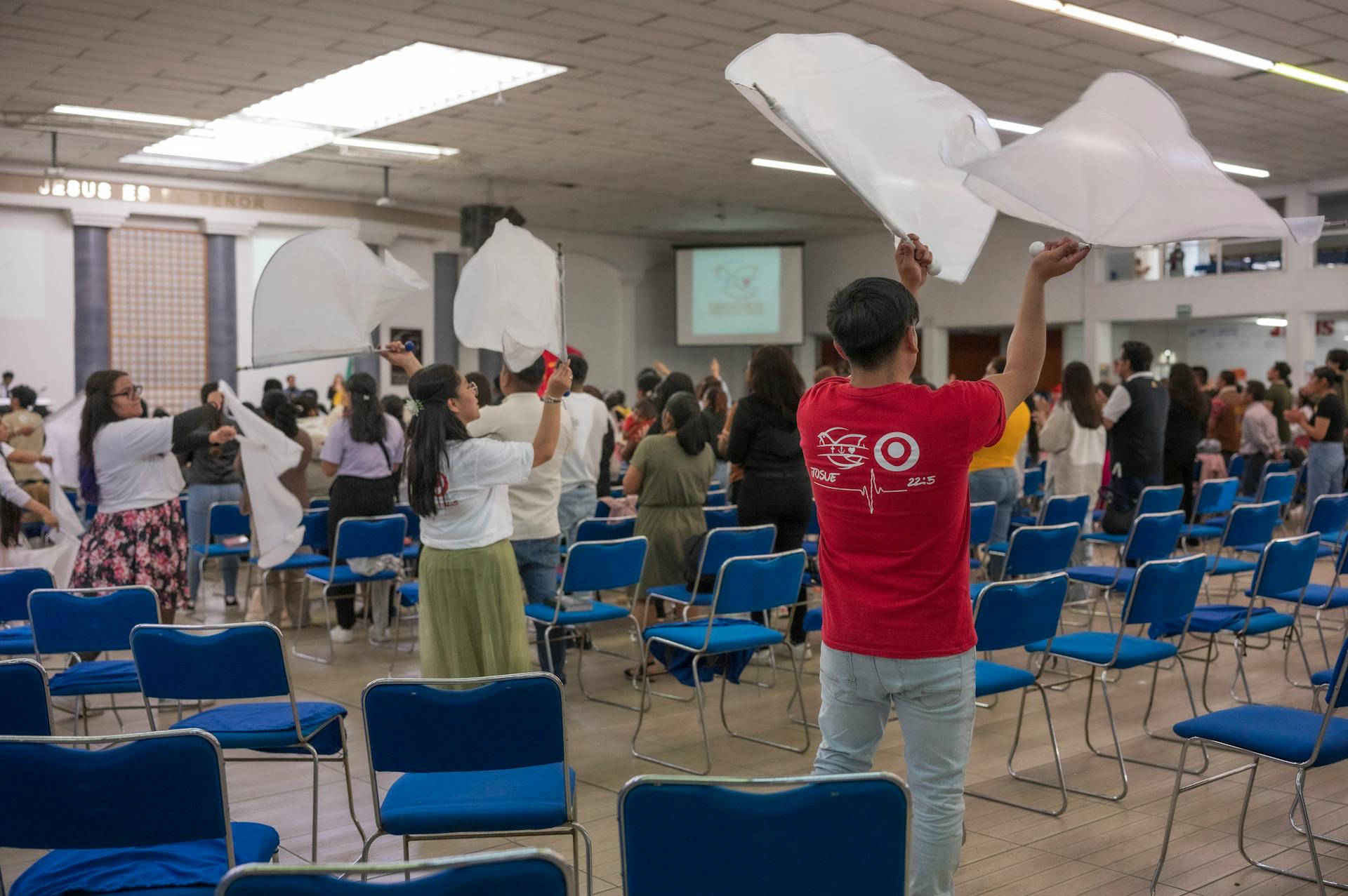 Indoor church gathering with people waving flags enthusiastically in a spacious auditorium.