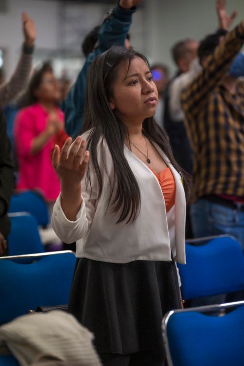 Free Young woman standing with raised hand during a religious gathering indoors. Stock Photo