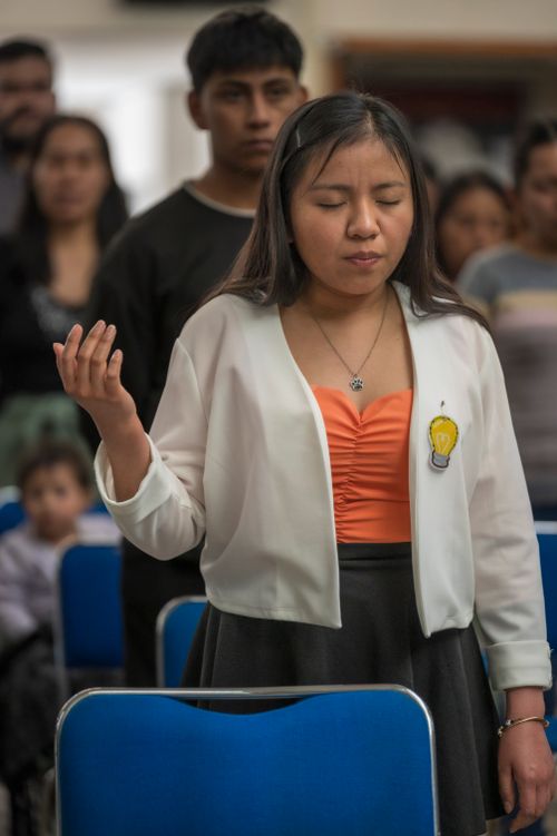 Free Young woman standing with eyes closed and hand raised in a spiritual gathering, expressing faith. Stock Photo