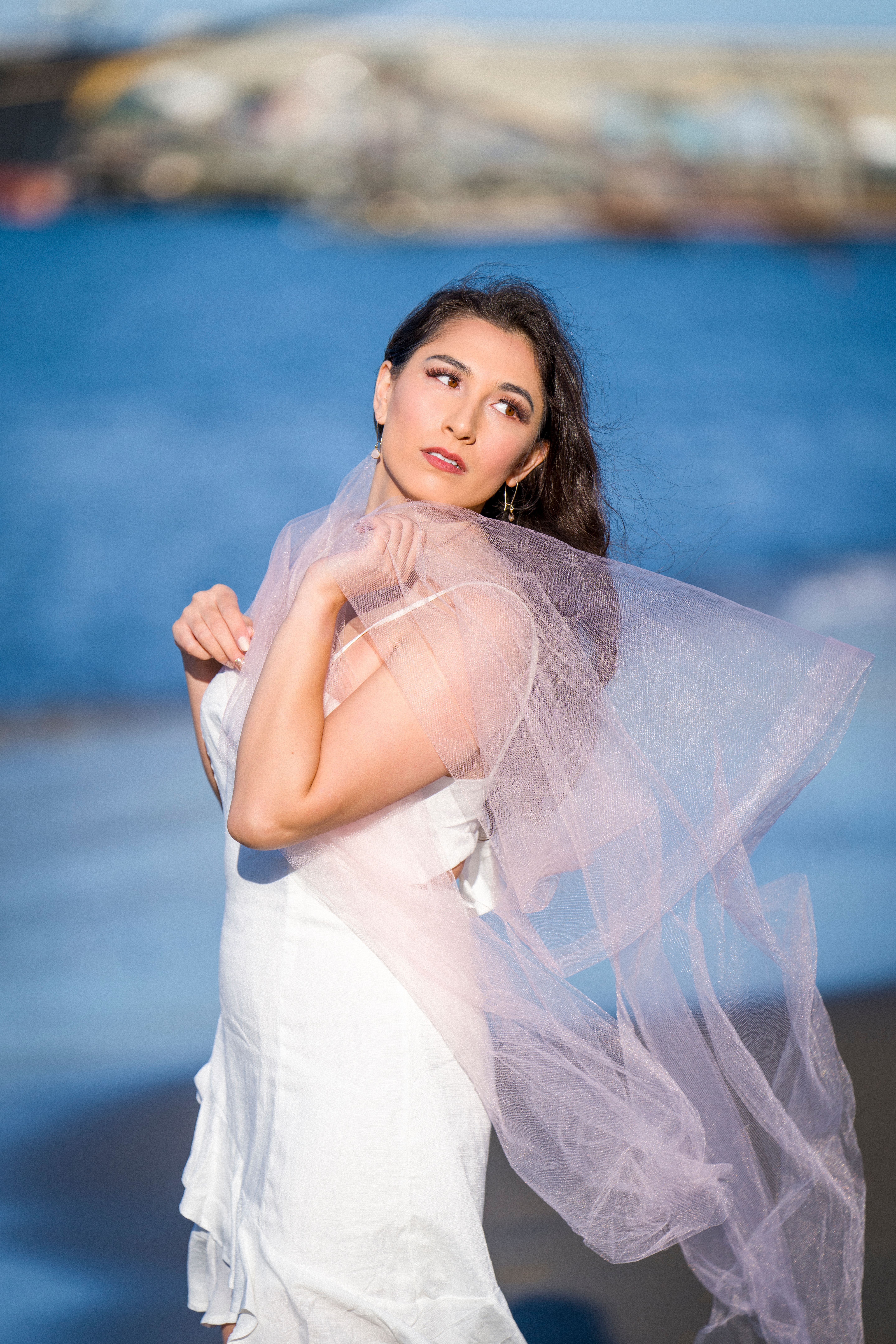 A captivating portrait of a woman in a flowing white dress and veil by the beach.