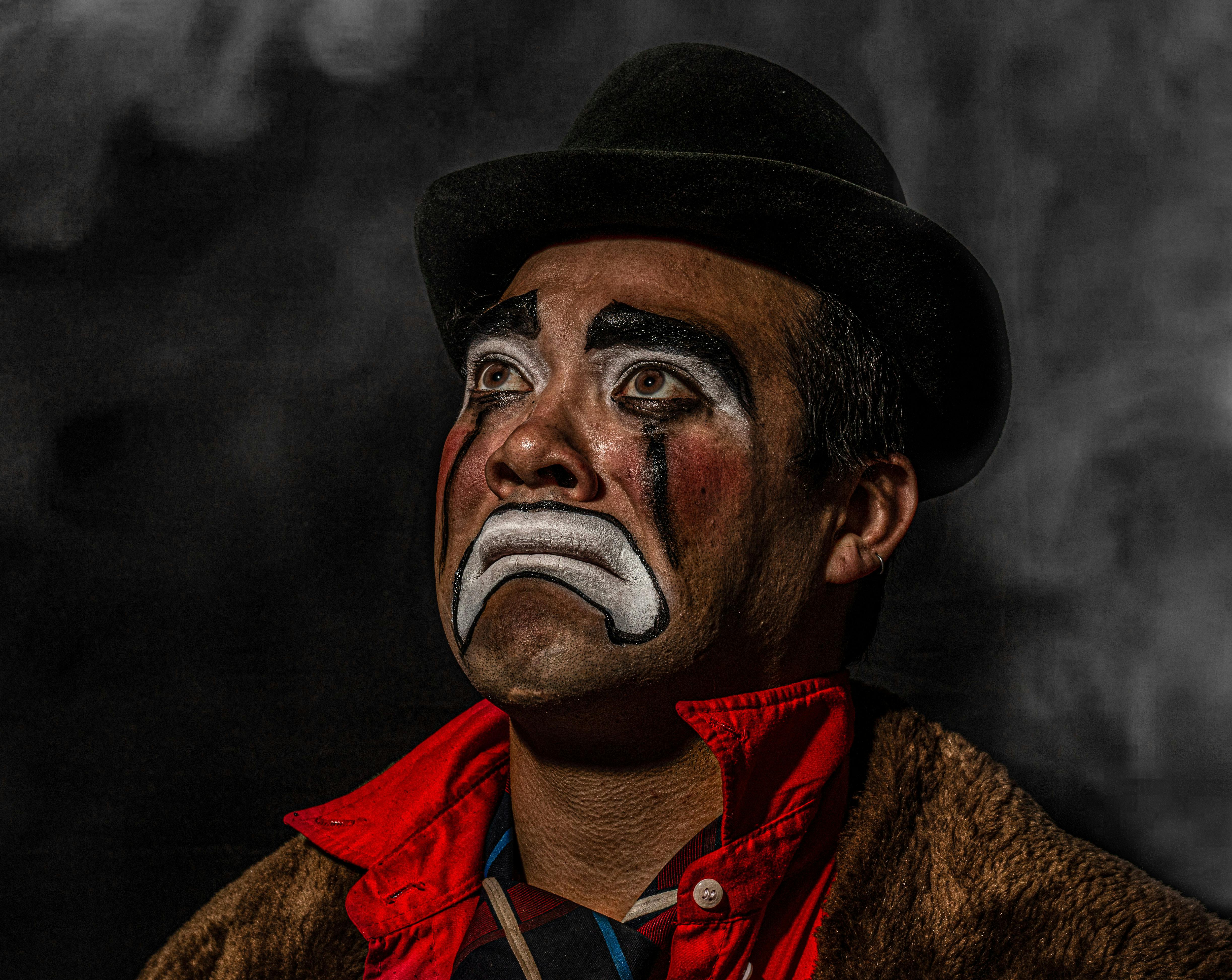 Close-up studio portrait of a sad clown with painted face looking upwards, capturing deep emotion.