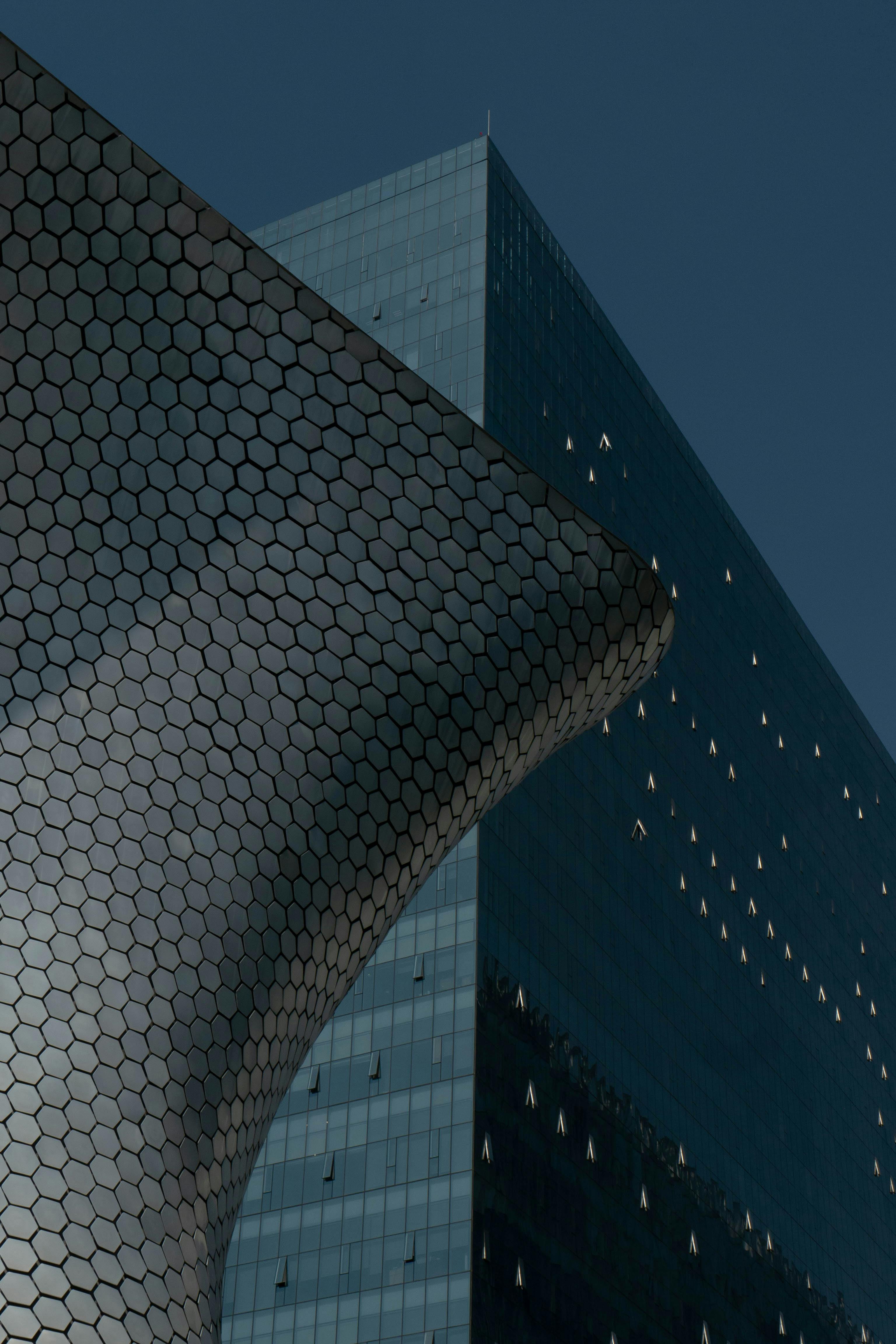 Dynamic perspective of a modern building featuring a hexagonal patterned facade against a sleek glass structure.