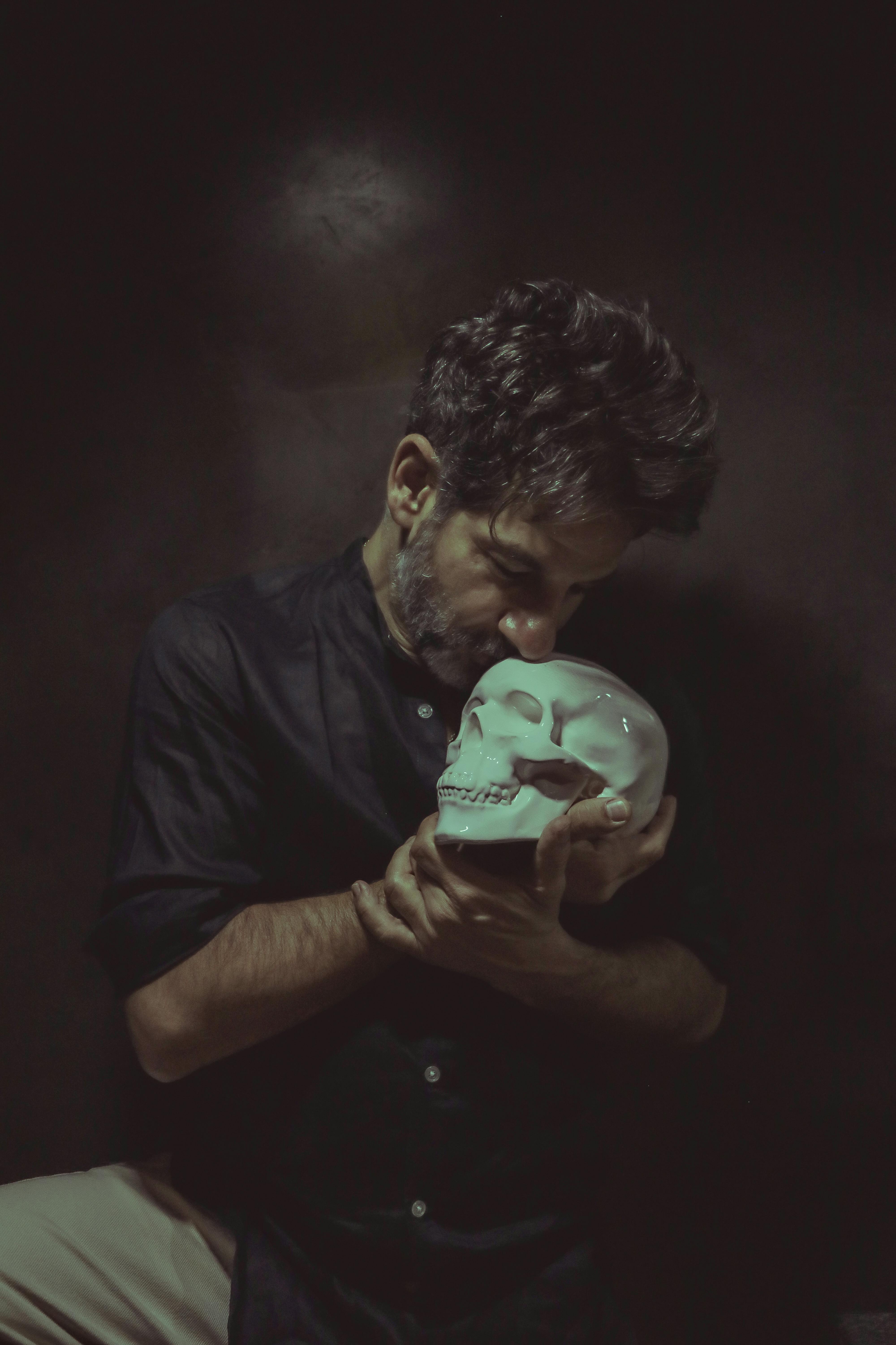 A man holds a skull in a moody, dark ambiance, creating an eerie and introspective vibe.