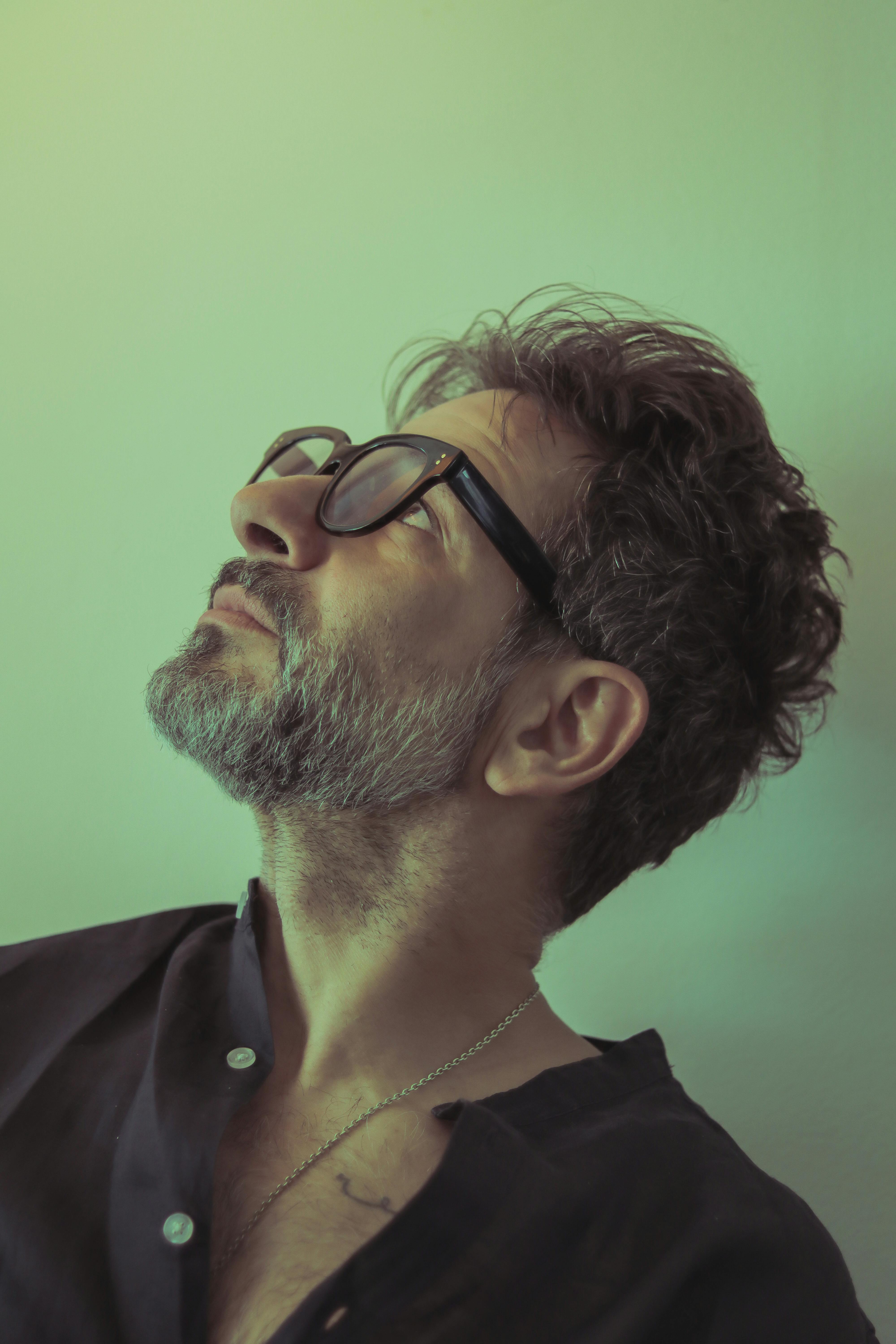 Portrait of a man with beard and glasses, looking up, captured in a studio setting.