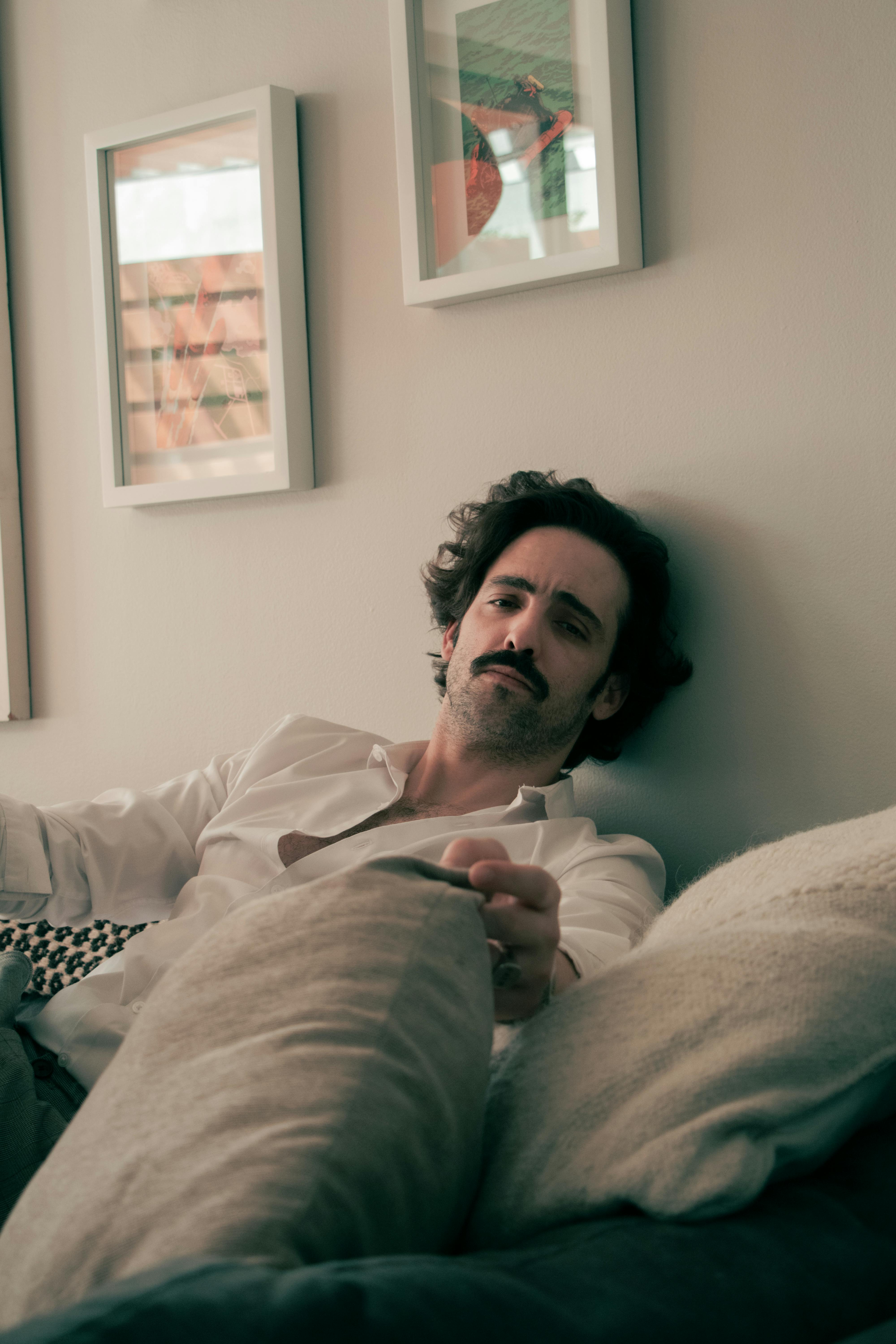 Casual portrait of a man with mustache lounging on a sofa with cushions in a cozy setting.