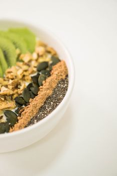 A vibrant smoothie bowl with kiwi, nuts, seeds, and chia on a neutral background.