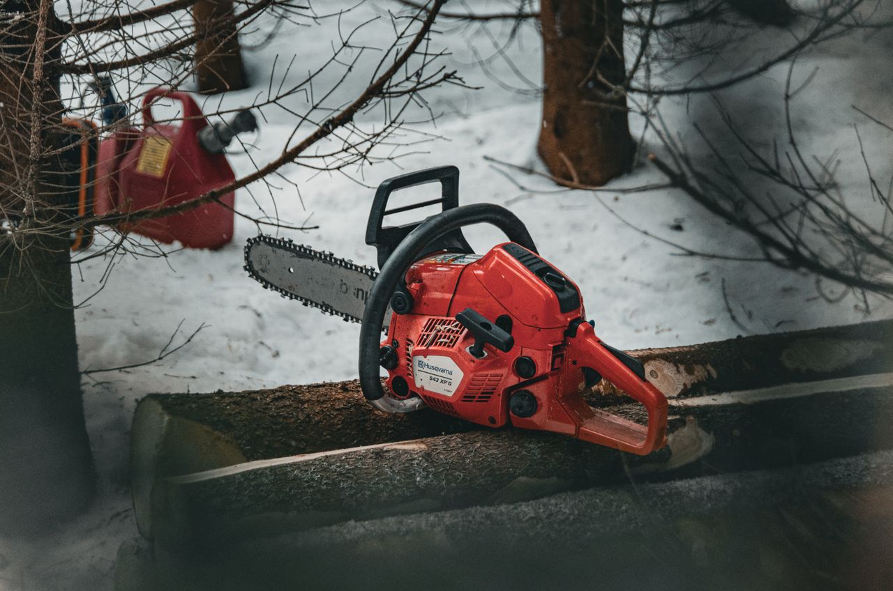 red chainsaw resting on snow covered tree logs in a winter forest sett