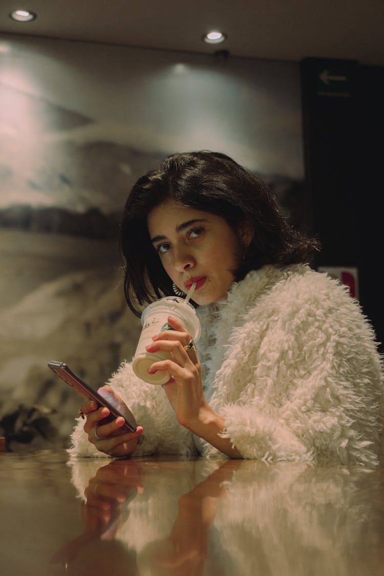 Woman Sipping A Drink From Starbucks And Using Her Phone