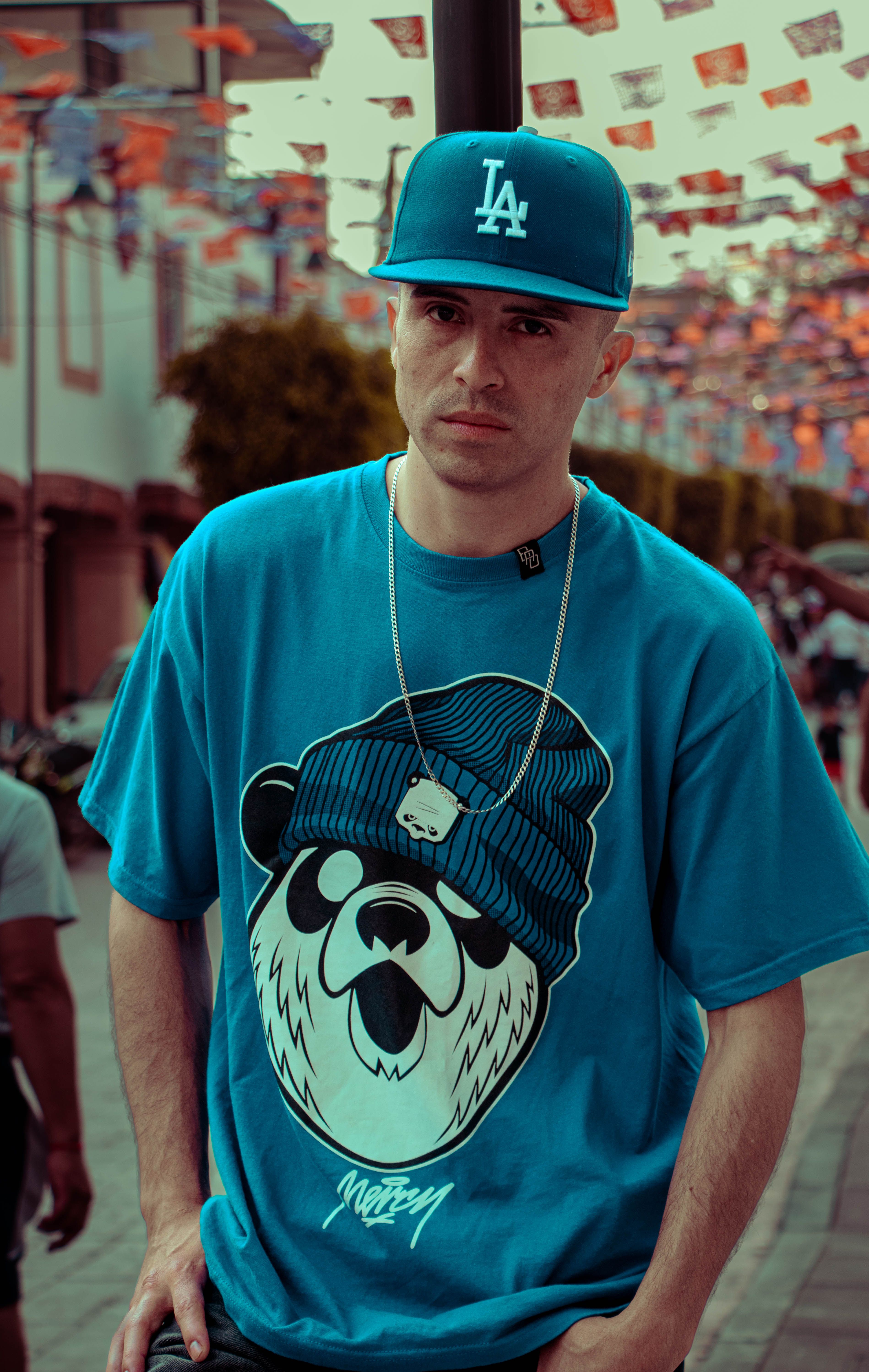 Portrait of a stylish young man in an urban setting wearing a blue graphic t-shirt and cap.