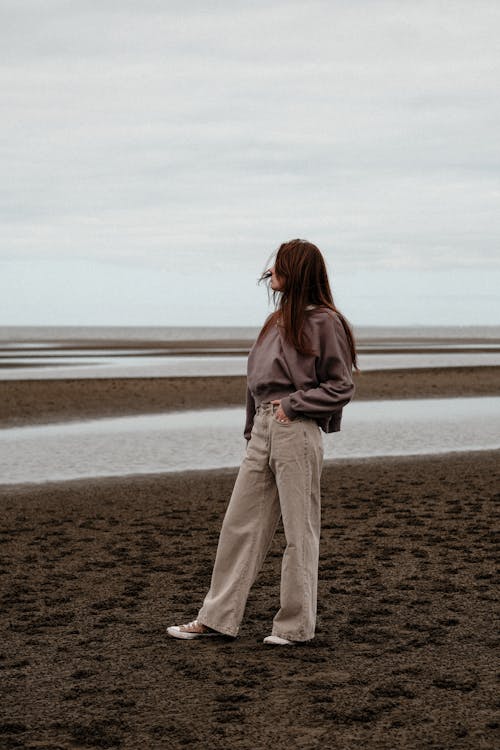 A woman standing on the beach in a beige pantsuit