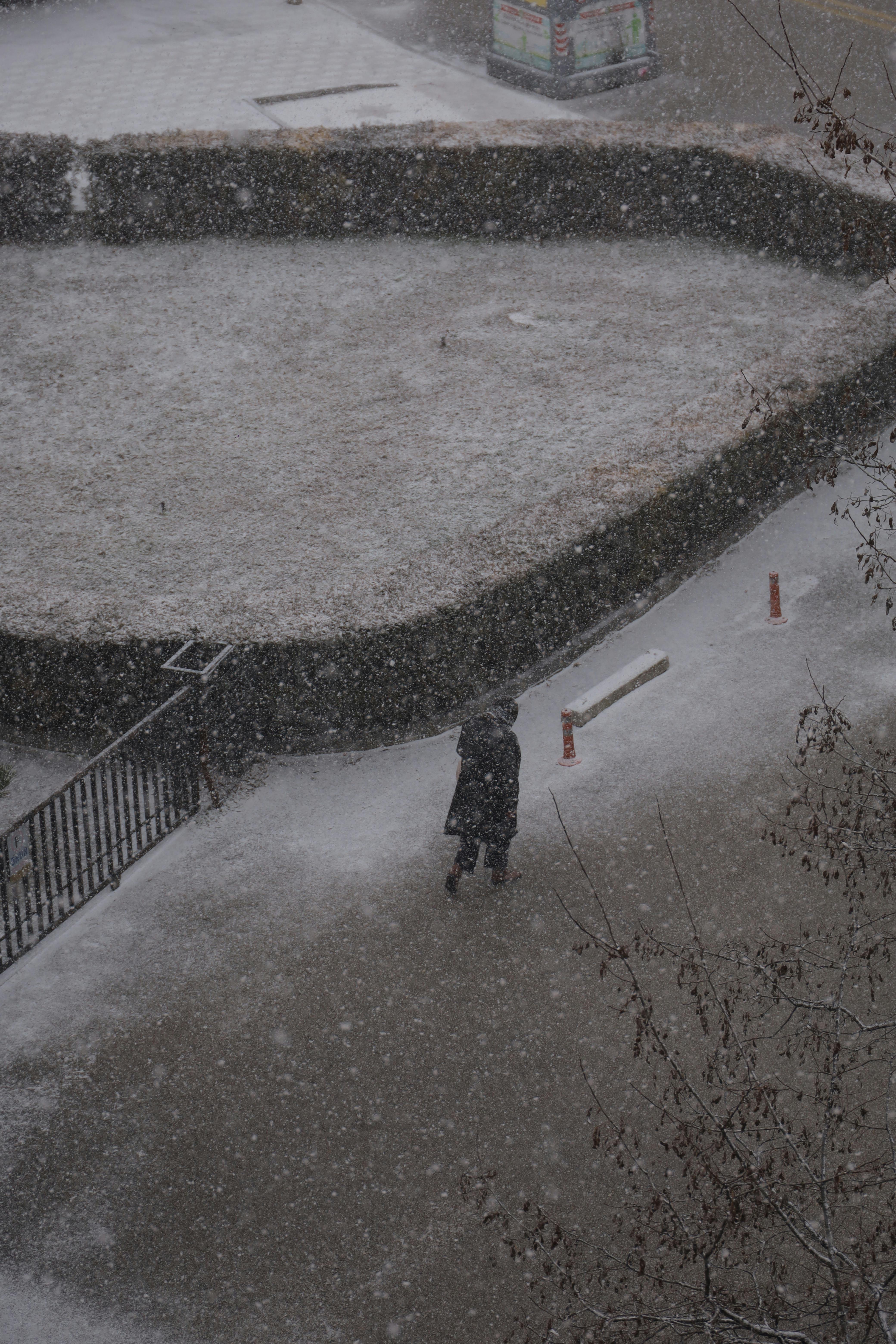 A lone person walks through a snowy city street, captured in an aerial view during a snowstorm.