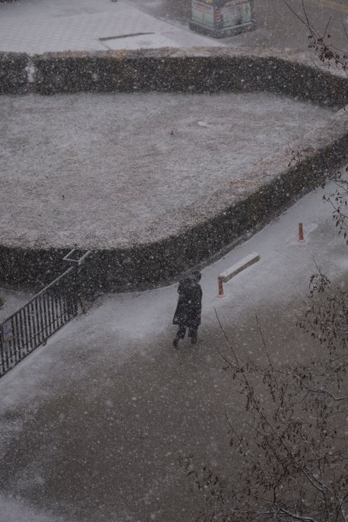 Free A lone person walks through a snowy city street, captured in an aerial view during a snowstorm. Stock Photo