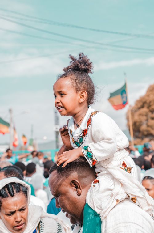 Free Smiling child on father's shoulders at a vibrant cultural festival outdoors. Stock Photo